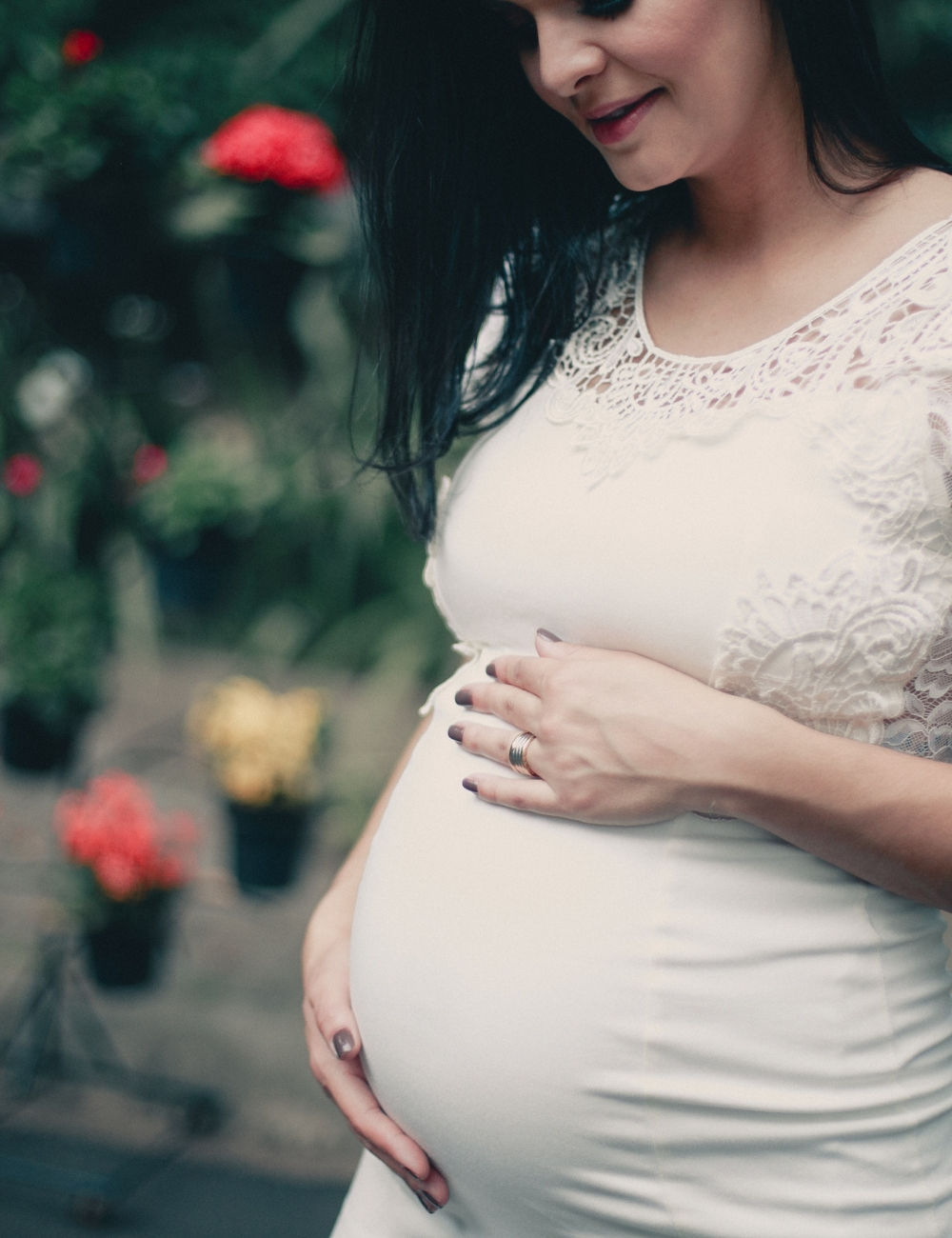 A fancily dressed pregnant woman holding her belly with flowers behind her