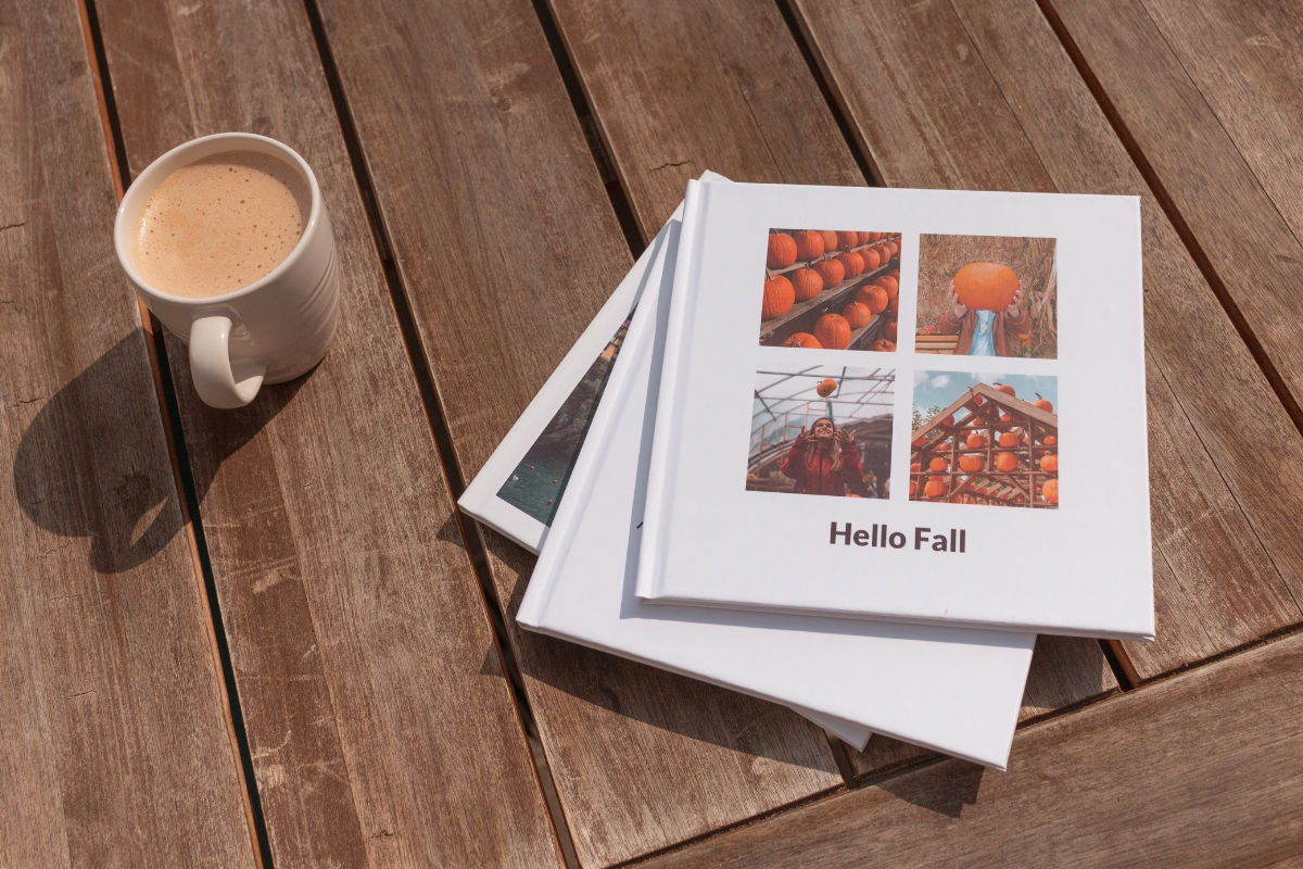 A stack of photo books with the title "Hello Fall" next to a warm cup of coffee