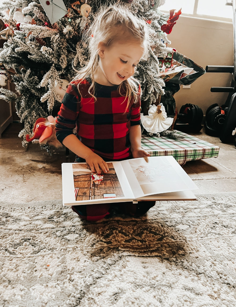 a young girl looking at a family photo book in front of a Christmas tree