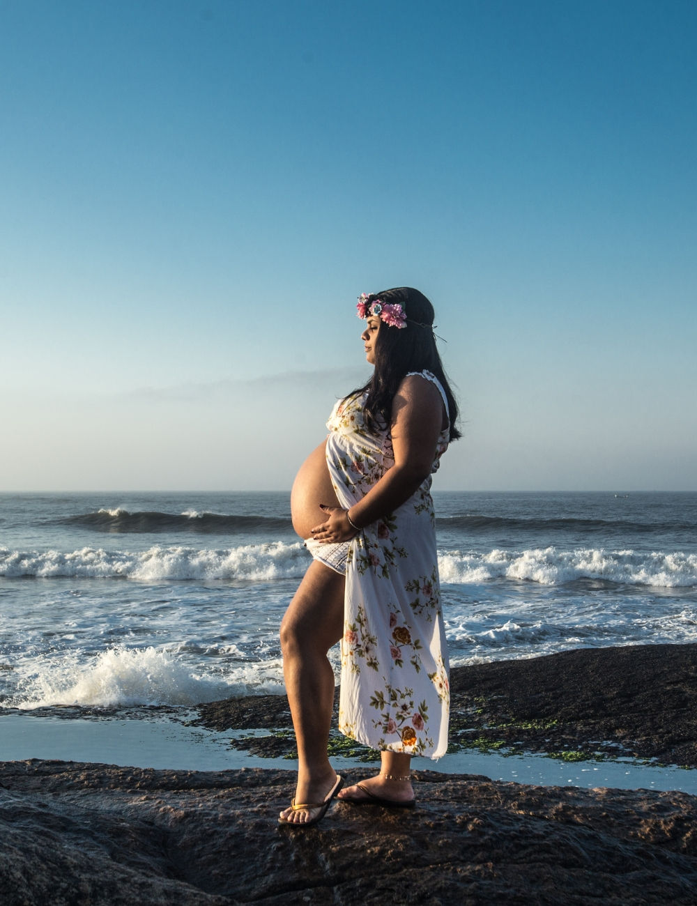 A pregnant woman holding her exposed belly at the beach