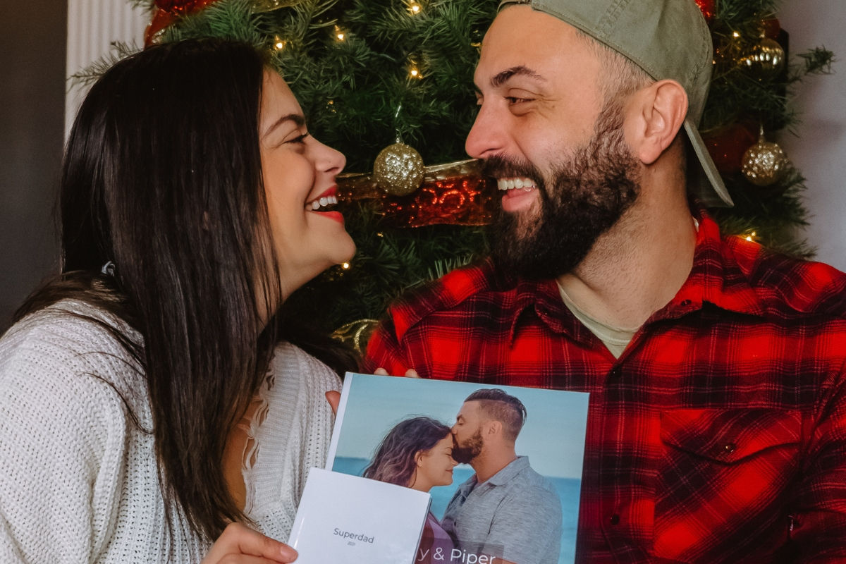 A couple smiling and looking at each other holding a photo book of their love story