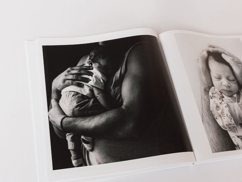 A SimplePrints Photo book open with black and white pictures of a father holding his baby