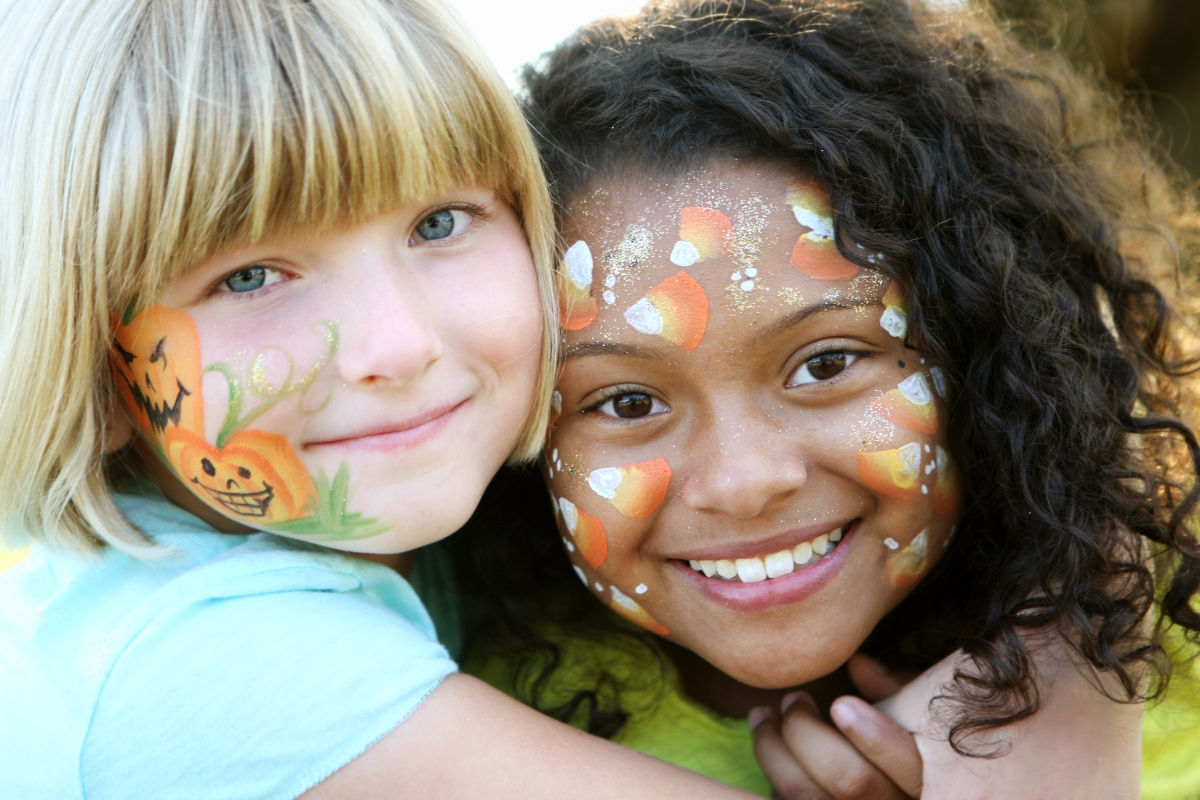 Two young girls hugging and smiling at the camera with fall themed face paint