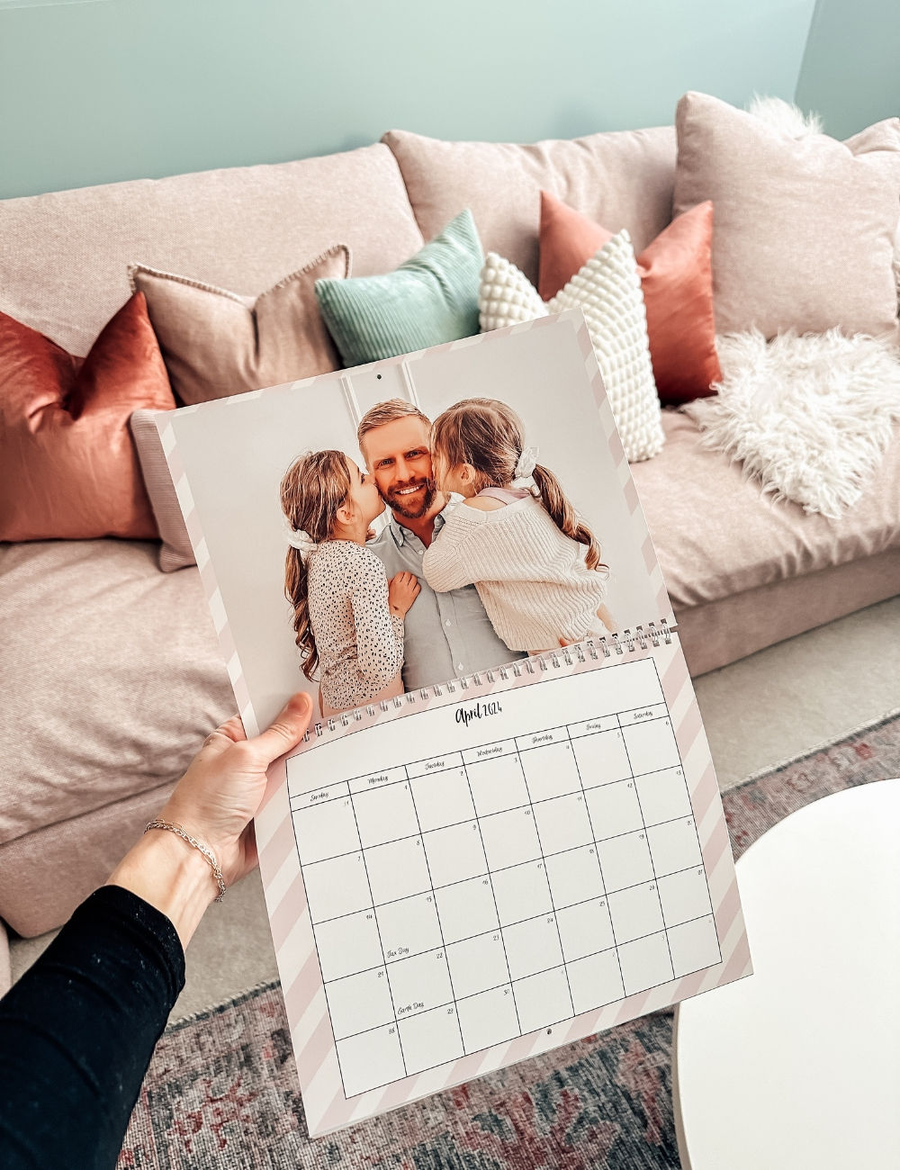 A wall calendar with a picture of a dad and his two daughters kissing each side of his cheek 