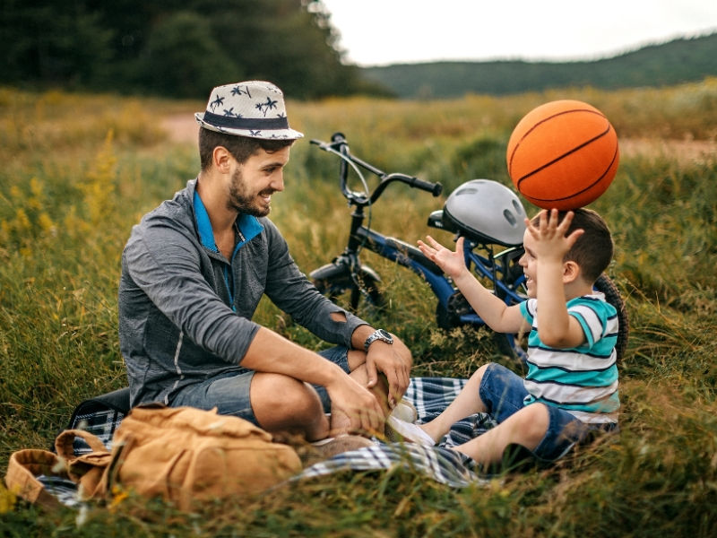 Dad and son on a field with a basketball and a bike