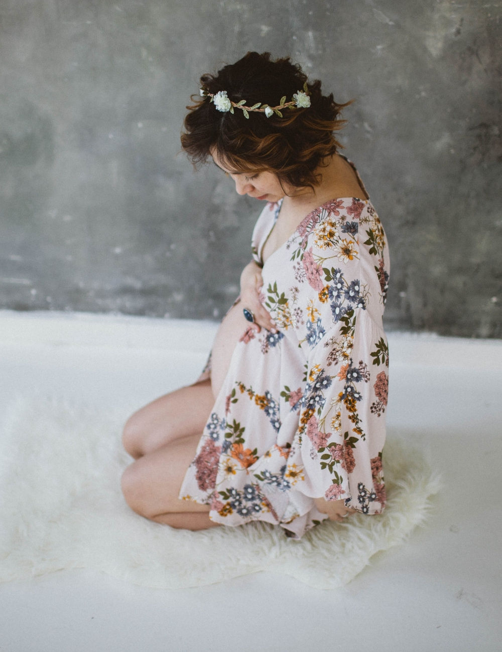 A pregnant woman kneeling on sheepskin in a studio with a flower kimono and crown