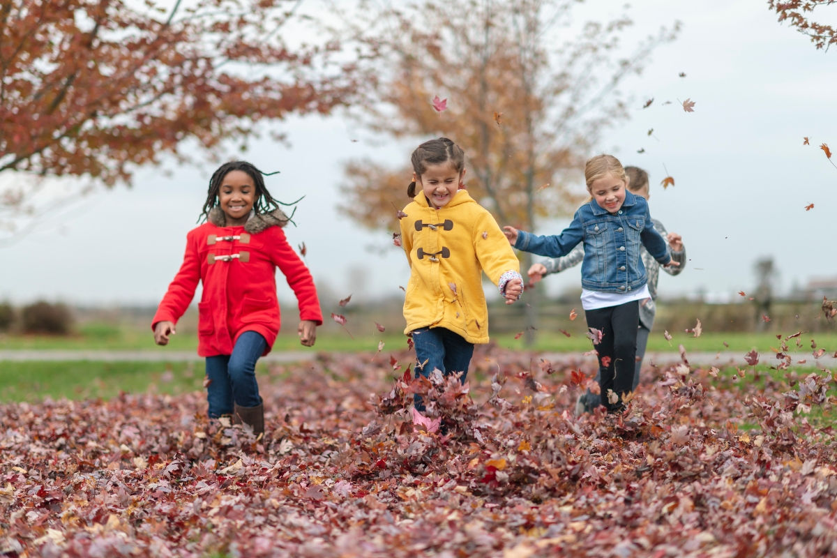 Three kids running through a a pile of leaves