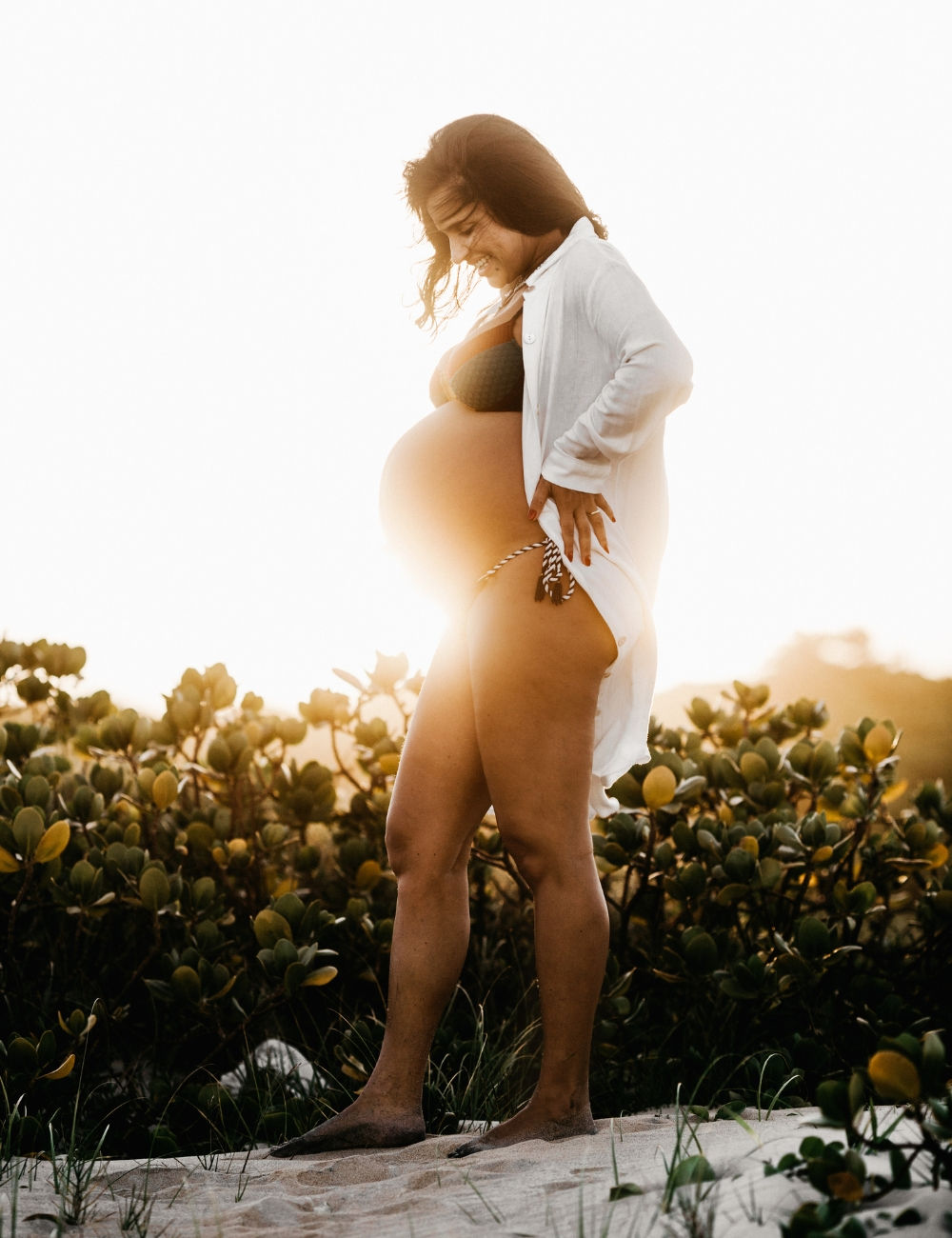 A women with an open collard shirt with the sun setting behind her belly