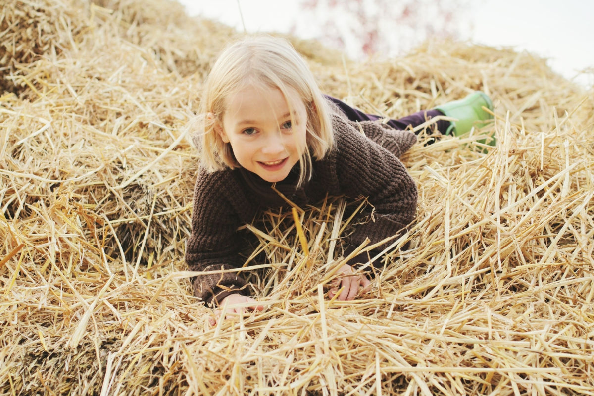 A girl climbing on hay bails smiling at the camera