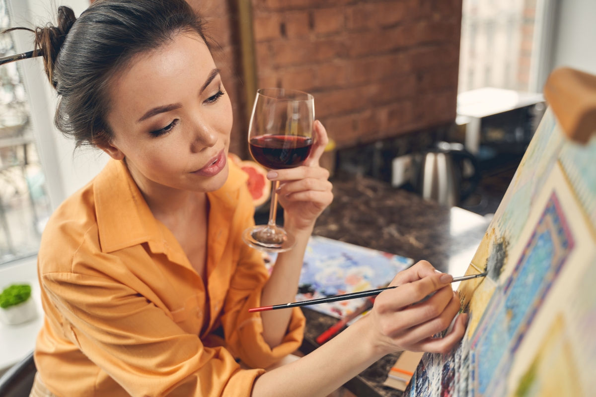 a woman paining on a canvas with a glass of wine