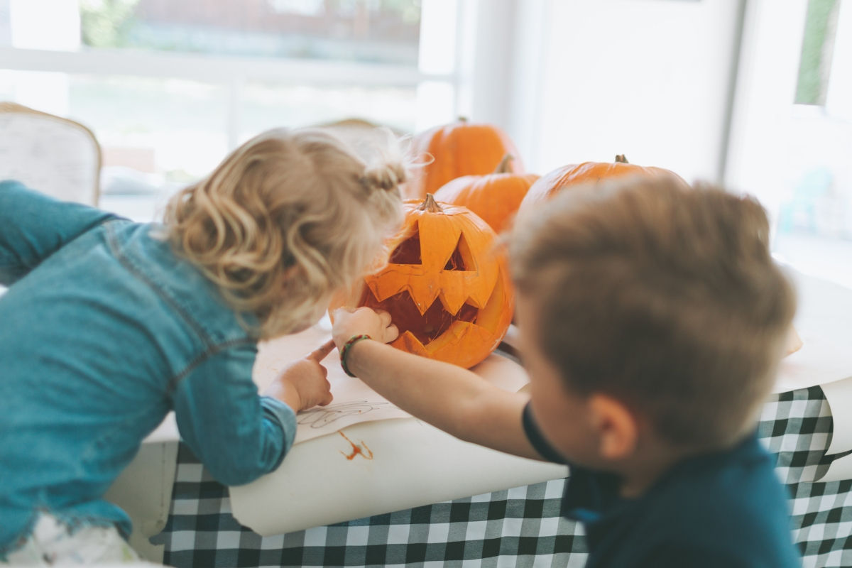 Two kids carving a pumpkin at a table