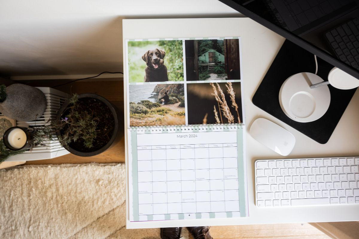 a wall calendar laying on the desk next to a computer featuring a collage of nature photos
