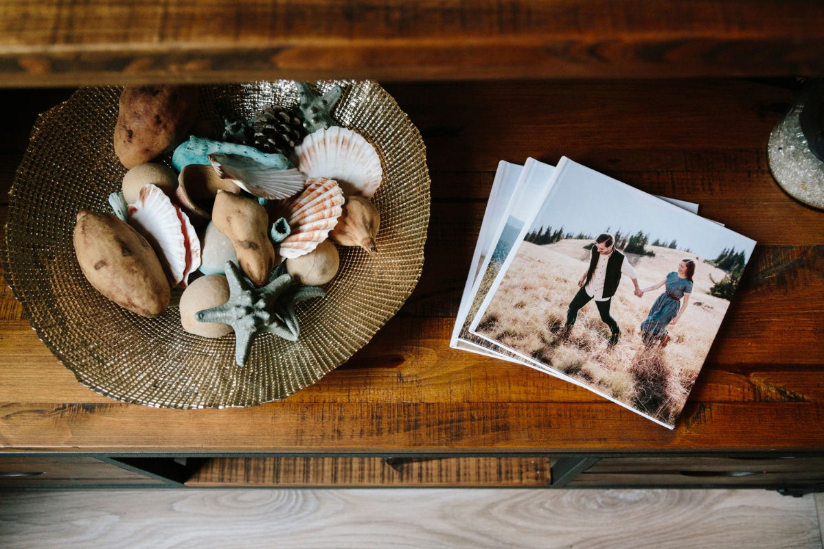 Photo books spread on a table with a couple holding hands on the cover, next to a bowl of seashells