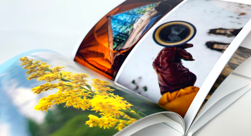 SimplePrints Photo book with vivid photos: close-up of yellow flowers, a person holding a coffee in snow, and a tent. Bright, vibrant colors.
